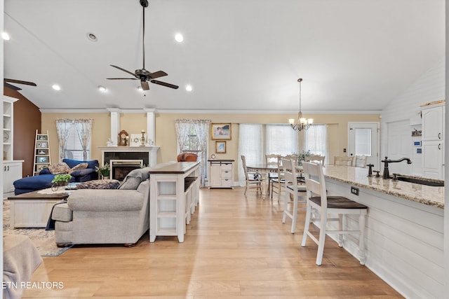 living room featuring ceiling fan with notable chandelier, light wood-type flooring, sink, and lofted ceiling