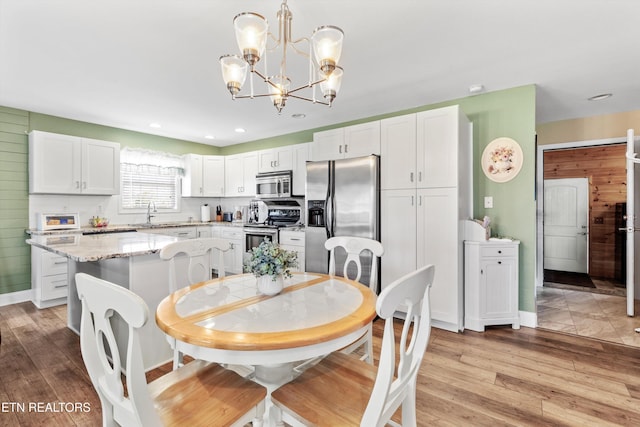 dining space with wood walls, light hardwood / wood-style floors, sink, and an inviting chandelier