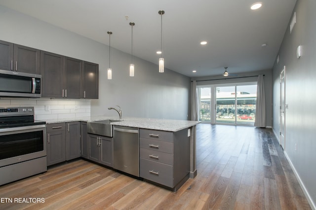 kitchen featuring sink, light stone counters, kitchen peninsula, and appliances with stainless steel finishes