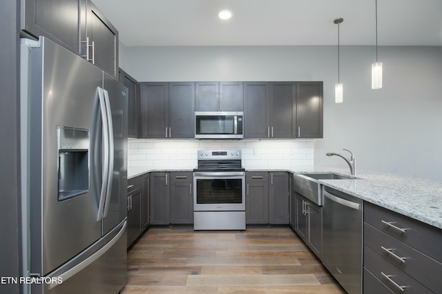 kitchen with stainless steel appliances, light stone counters, tasteful backsplash, hanging light fixtures, and dark wood-type flooring