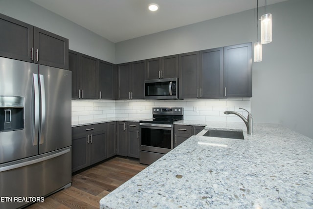 kitchen with light stone countertops, pendant lighting, backsplash, appliances with stainless steel finishes, and sink