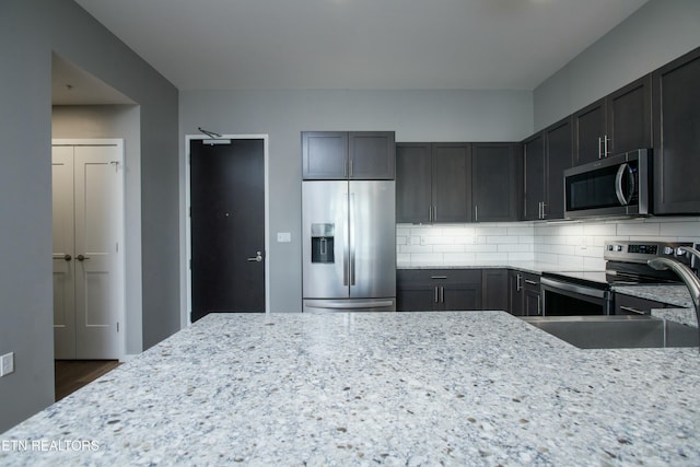 kitchen featuring light stone counters, sink, tasteful backsplash, appliances with stainless steel finishes, and dark brown cabinetry