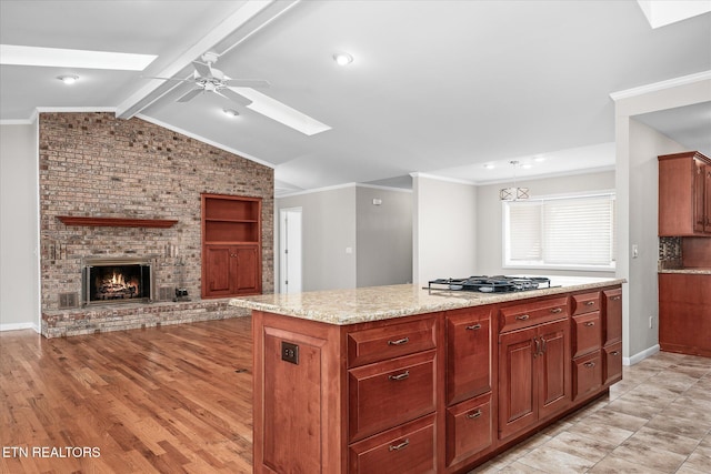 kitchen with light stone countertops, hanging light fixtures, a kitchen island, stainless steel gas stovetop, and a fireplace