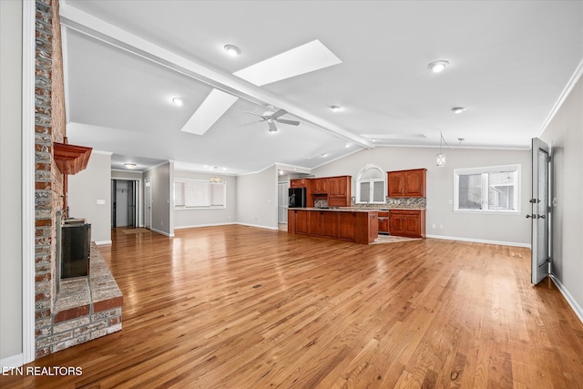 unfurnished living room featuring light hardwood / wood-style floors, a fireplace, lofted ceiling with skylight, and ceiling fan