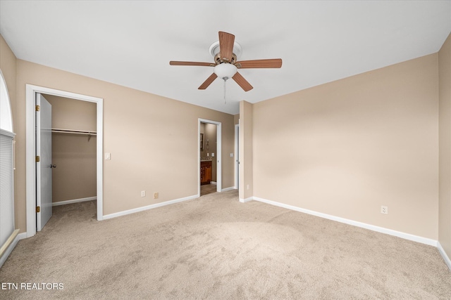 unfurnished bedroom with ceiling fan, a walk in closet, a closet, and light colored carpet