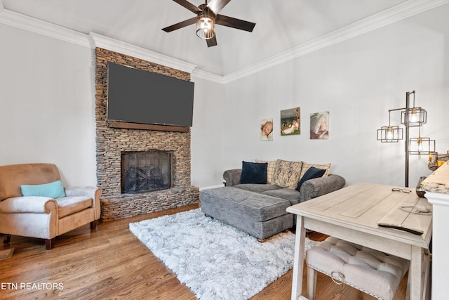 living room featuring ceiling fan, ornamental molding, hardwood / wood-style flooring, and a stone fireplace