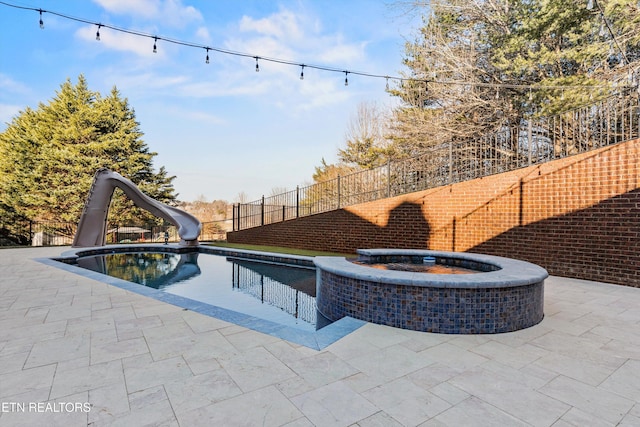 view of pool featuring a water slide, a patio, and an in ground hot tub