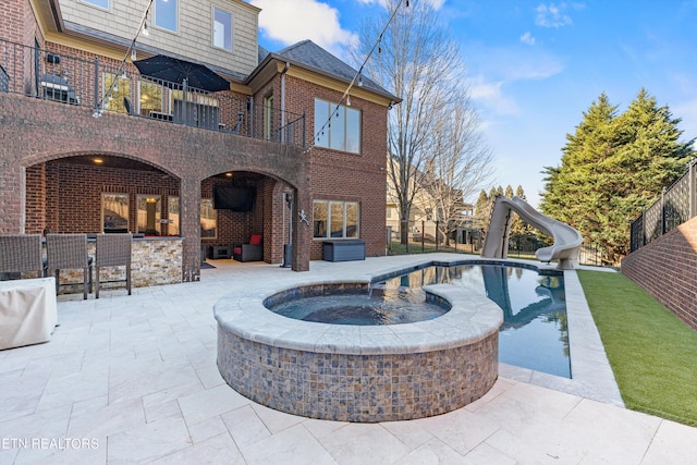 view of swimming pool with a water slide, a patio area, a bar, and an in ground hot tub