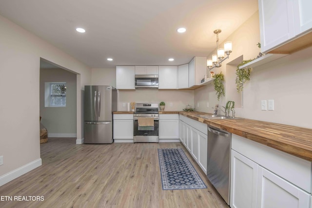 kitchen with stainless steel appliances, white cabinetry, hanging light fixtures, and sink