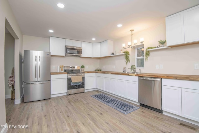 kitchen featuring butcher block countertops, a chandelier, decorative light fixtures, white cabinets, and appliances with stainless steel finishes