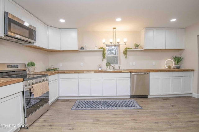 kitchen with hanging light fixtures, light hardwood / wood-style flooring, white cabinetry, butcher block counters, and stainless steel appliances