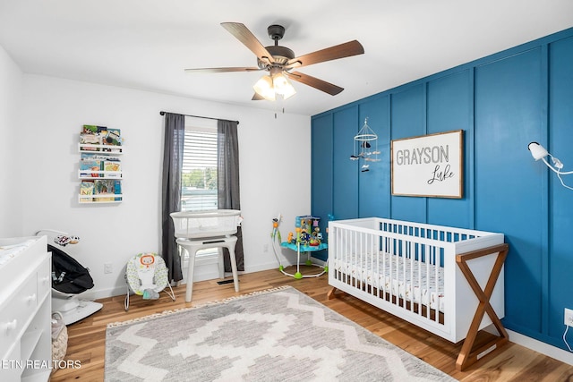 bedroom with hardwood / wood-style flooring, a nursery area, and ceiling fan