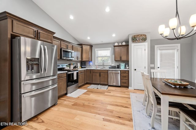 kitchen with stainless steel appliances, vaulted ceiling, a chandelier, light hardwood / wood-style floors, and hanging light fixtures