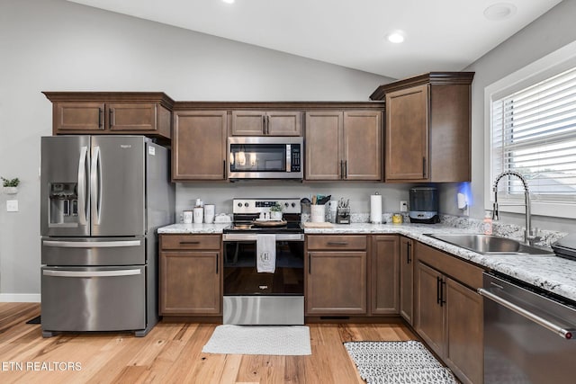 kitchen featuring lofted ceiling, sink, light hardwood / wood-style floors, light stone counters, and stainless steel appliances