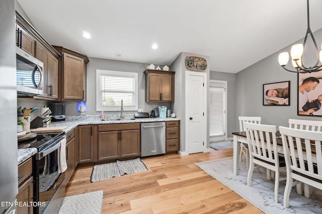 kitchen featuring light stone countertops, sink, stainless steel appliances, pendant lighting, and light wood-type flooring