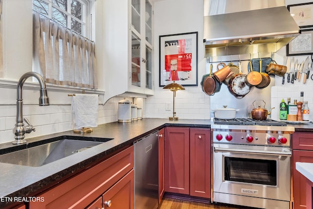 kitchen featuring tasteful backsplash, dark stone counters, wall chimney exhaust hood, stainless steel appliances, and sink