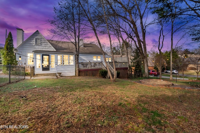 back house at dusk with a yard and a wooden deck