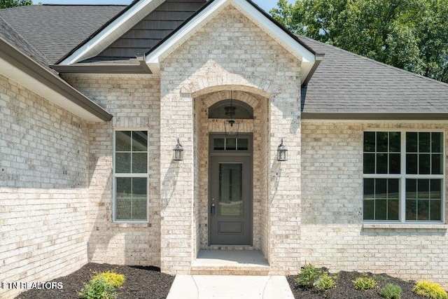 view of exterior entry featuring brick siding and roof with shingles