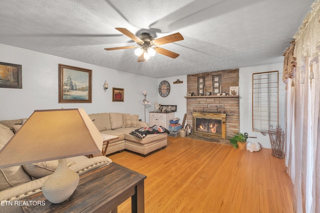 living room featuring ceiling fan, a fireplace, a textured ceiling, and light wood-type flooring