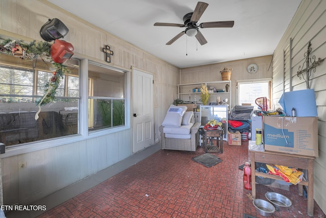 interior space featuring ceiling fan and wooden walls