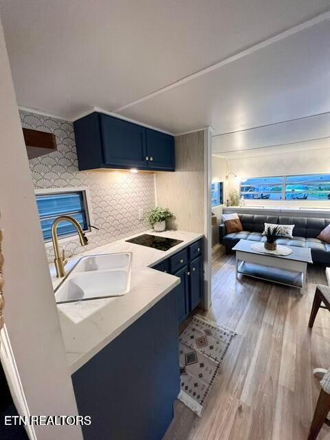 kitchen with sink, decorative backsplash, black electric cooktop, blue cabinetry, and light hardwood / wood-style floors