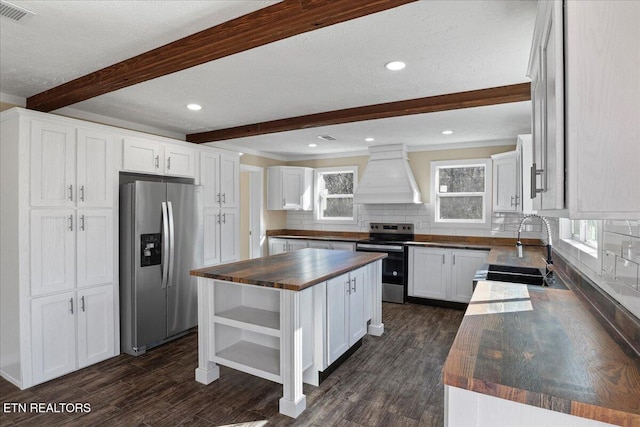 kitchen featuring wood counters, appliances with stainless steel finishes, premium range hood, white cabinets, and a center island