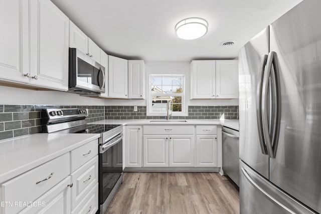 kitchen with sink, white cabinets, stainless steel appliances, and light hardwood / wood-style floors