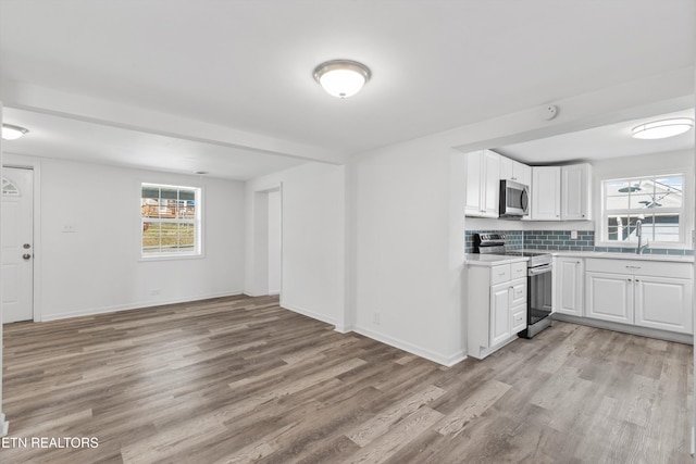 kitchen with sink, decorative backsplash, light hardwood / wood-style floors, white cabinetry, and stainless steel appliances