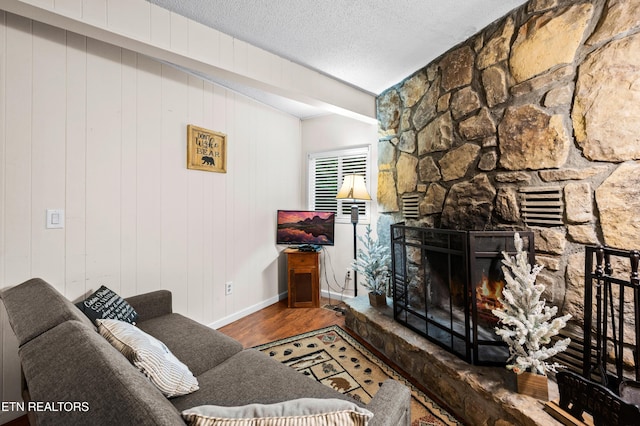 living room with a stone fireplace, wood-type flooring, and a textured ceiling