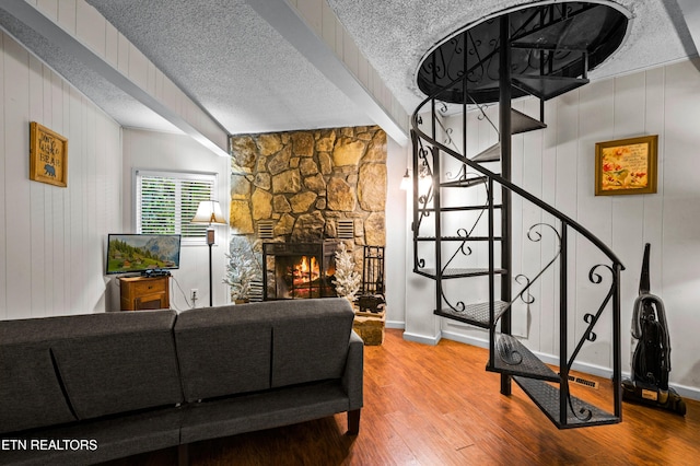 living room featuring wood-type flooring, a stone fireplace, and a textured ceiling