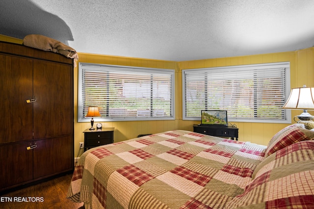 bedroom featuring multiple windows, dark hardwood / wood-style floors, wooden walls, and a textured ceiling