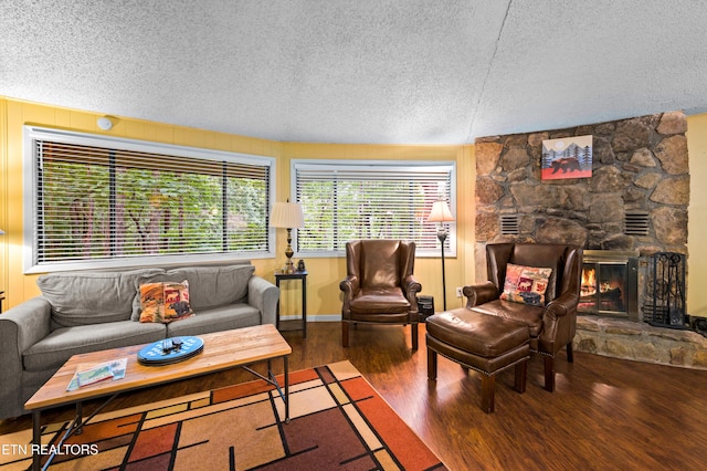 living room with a stone fireplace, wood-type flooring, and a textured ceiling