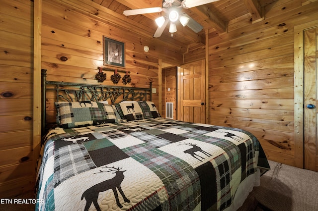 carpeted bedroom with beamed ceiling, ceiling fan, wood ceiling, and wooden walls