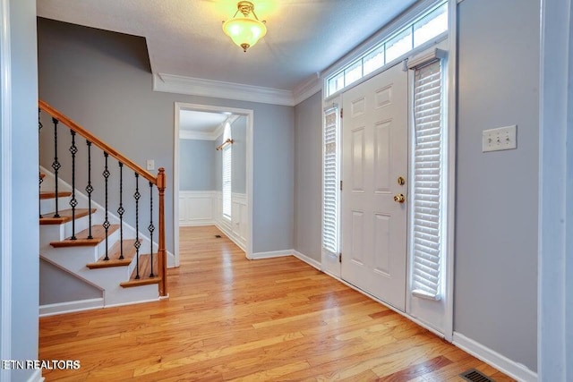 foyer featuring light wood finished floors, stairs, and ornamental molding