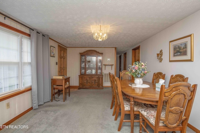 dining space featuring light carpet, a textured ceiling, wooden walls, and a notable chandelier