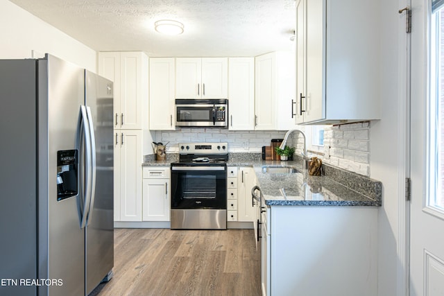 kitchen with stainless steel appliances, sink, white cabinets, dark stone countertops, and light hardwood / wood-style flooring