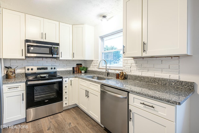 kitchen featuring stainless steel appliances, stone countertops, white cabinetry, and sink