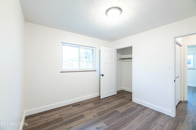 unfurnished bedroom with dark wood-type flooring, a textured ceiling, a closet, and multiple windows