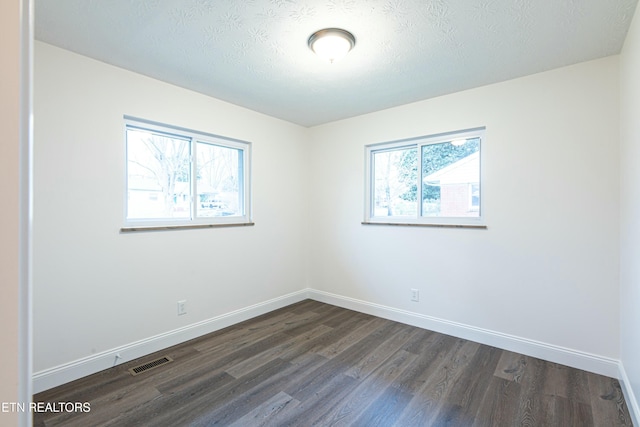 empty room featuring a textured ceiling, dark hardwood / wood-style flooring, and plenty of natural light