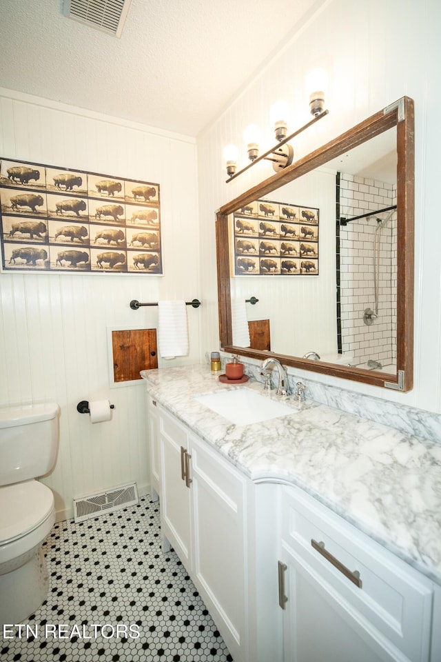 bathroom featuring wooden walls, tile patterned flooring, vanity, tiled shower, and a textured ceiling