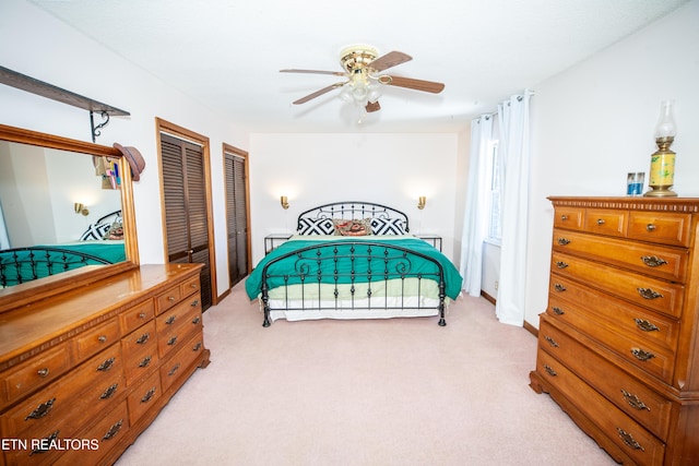 bedroom with two closets, light colored carpet, and ceiling fan