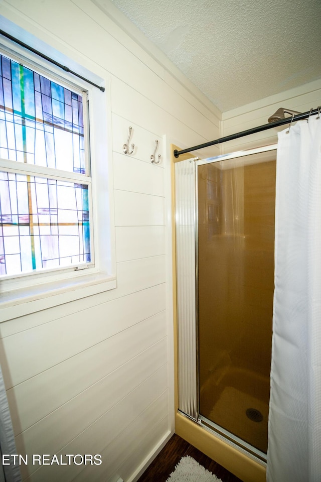 bathroom featuring wood walls, a textured ceiling, and walk in shower