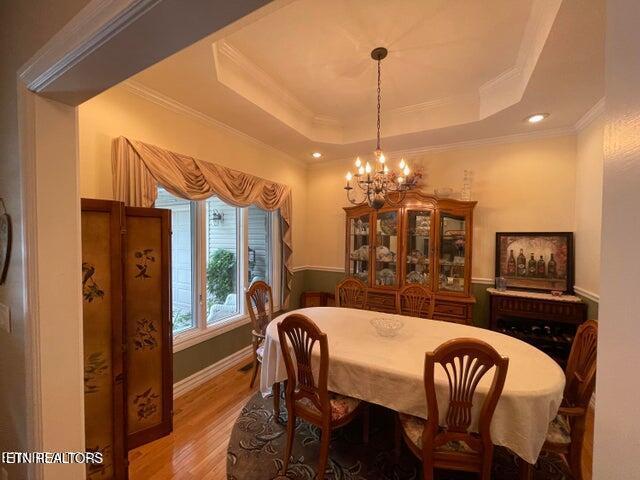 dining space featuring a tray ceiling, crown molding, light wood-style flooring, and an inviting chandelier