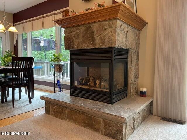 room details with a chandelier, visible vents, a stone fireplace, and wood finished floors