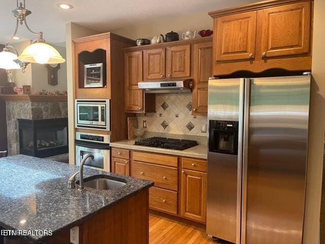 kitchen with appliances with stainless steel finishes, brown cabinetry, a sink, and under cabinet range hood