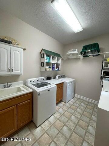 laundry room featuring cabinet space, washing machine and dryer, a textured ceiling, and a sink