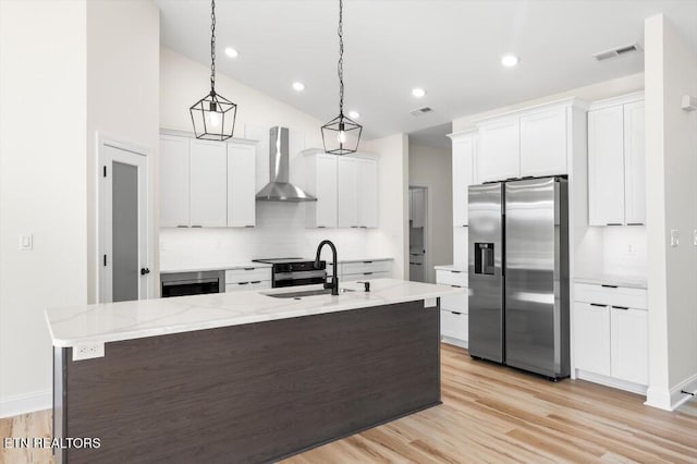 kitchen featuring sink, wall chimney range hood, stainless steel refrigerator with ice dispenser, pendant lighting, and white cabinets