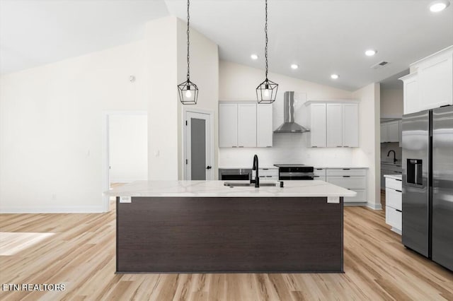 kitchen featuring white cabinets, wall chimney range hood, sink, appliances with stainless steel finishes, and decorative light fixtures