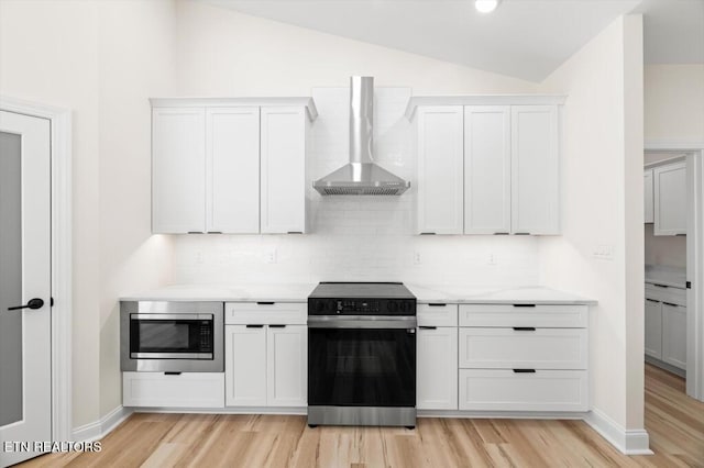 kitchen featuring wall chimney range hood, light hardwood / wood-style flooring, vaulted ceiling, white cabinetry, and stainless steel appliances