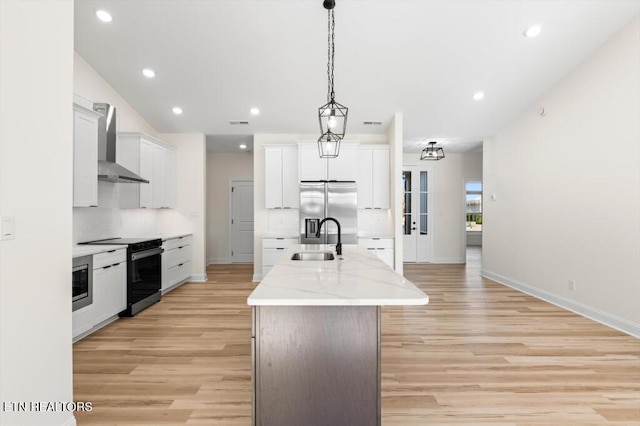 kitchen featuring a center island with sink, white cabinetry, wall chimney range hood, and appliances with stainless steel finishes